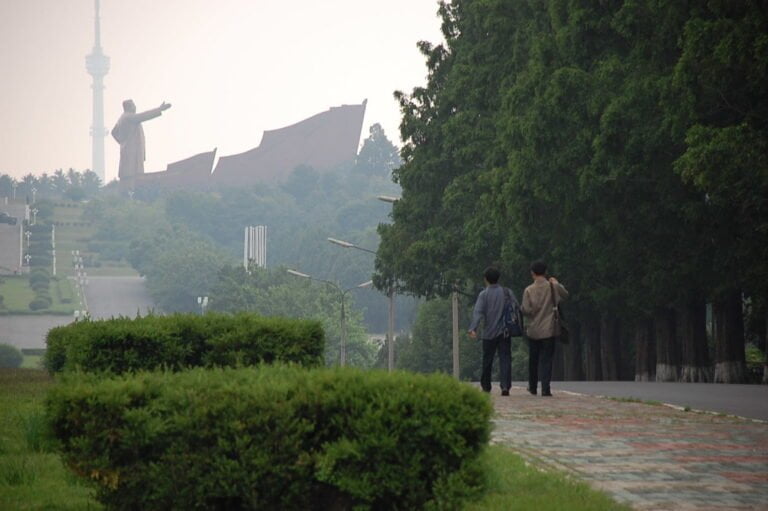 Two people walking down a path with statues and structures in hazy distance.