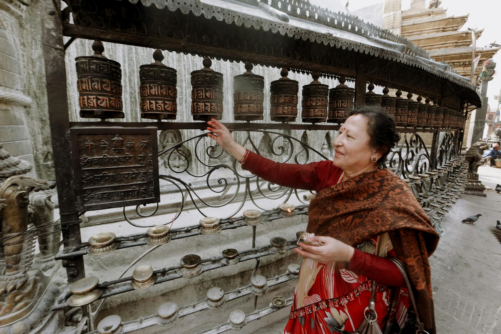 A woman in traditional attire is spinning prayer wheels at a Buddhist temple.