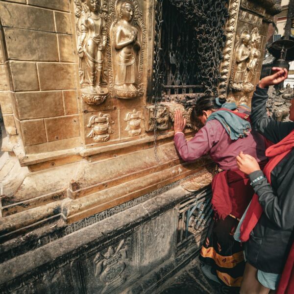 A woman and a child touching and observing a golden temple wall adorned with bas-relief sculptures.