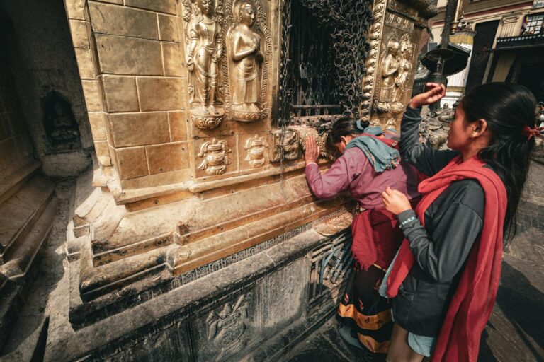 A woman and a child touching and observing a golden temple wall adorned with bas-relief sculptures.