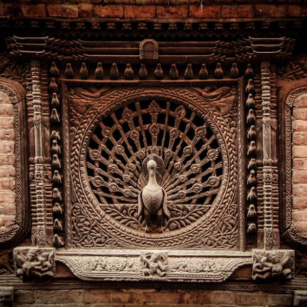 Intricately carved traditional wooden window with a peacock design on a brick wall.
