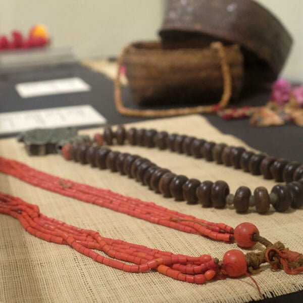Traditional necklaces displayed on a burlap surface with cultural artifacts blurred in the background.