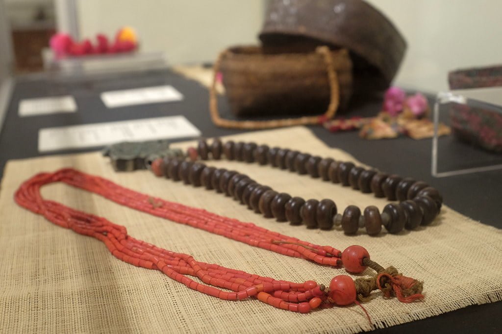 Traditional necklaces displayed on a burlap surface with cultural artifacts blurred in the background.