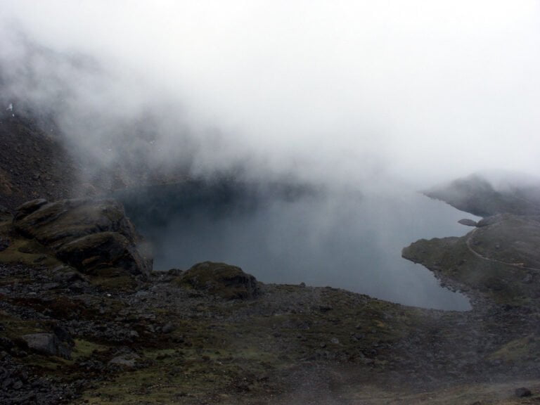 A misty mountain landscape with a serene lake partially obscured by low-hanging clouds.