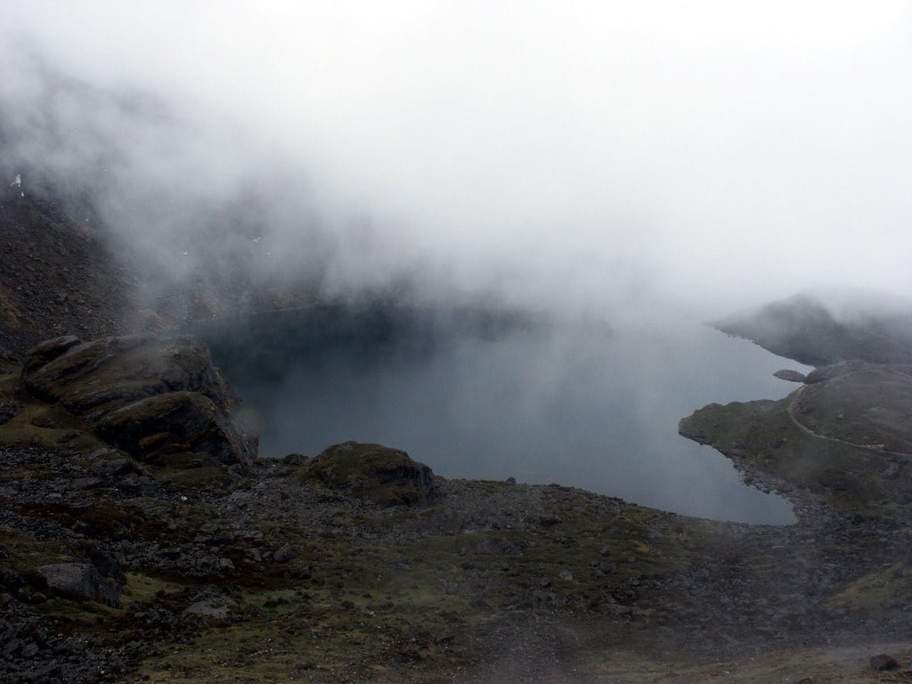 A misty mountain landscape with a serene lake partially obscured by low-hanging clouds.