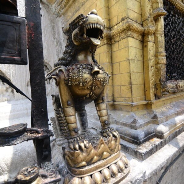 Bronze mythological lion-like statues flanking the corner of a golden religious shrine with intricate designs, set against a backdrop of other architectural elements.
