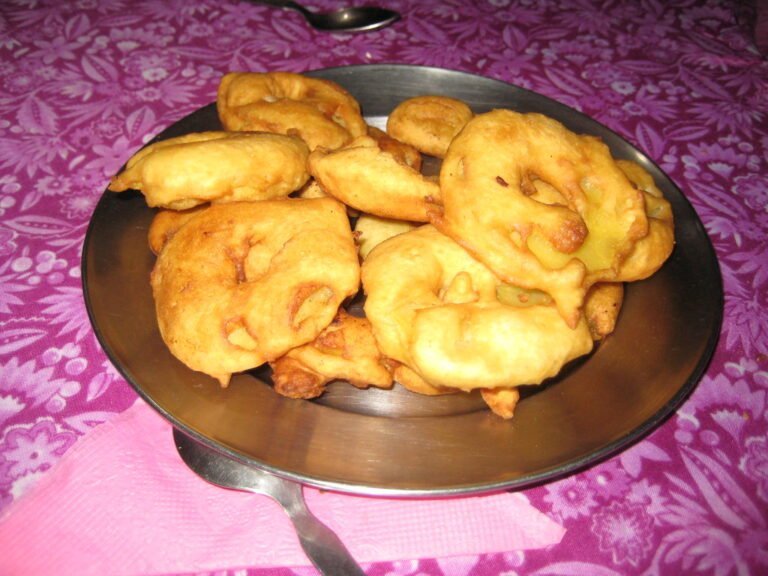 A plate of fried golden-brown fritters on a pink patterned tablecloth.