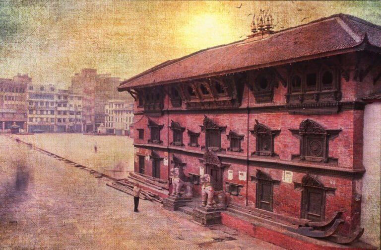 Alt text: An aged textured photograph of a traditional red brick building with detailed wood carvings and figures, possibly a temple, in an open square, with sunlight casting a warm glow on the scene.