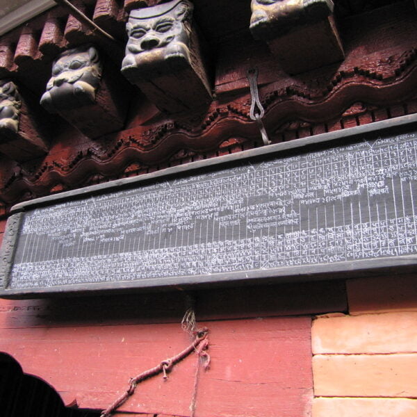 A black stone tablet with intricate inscriptions hanging on a red wall, with traditional wooden carved faces above it.