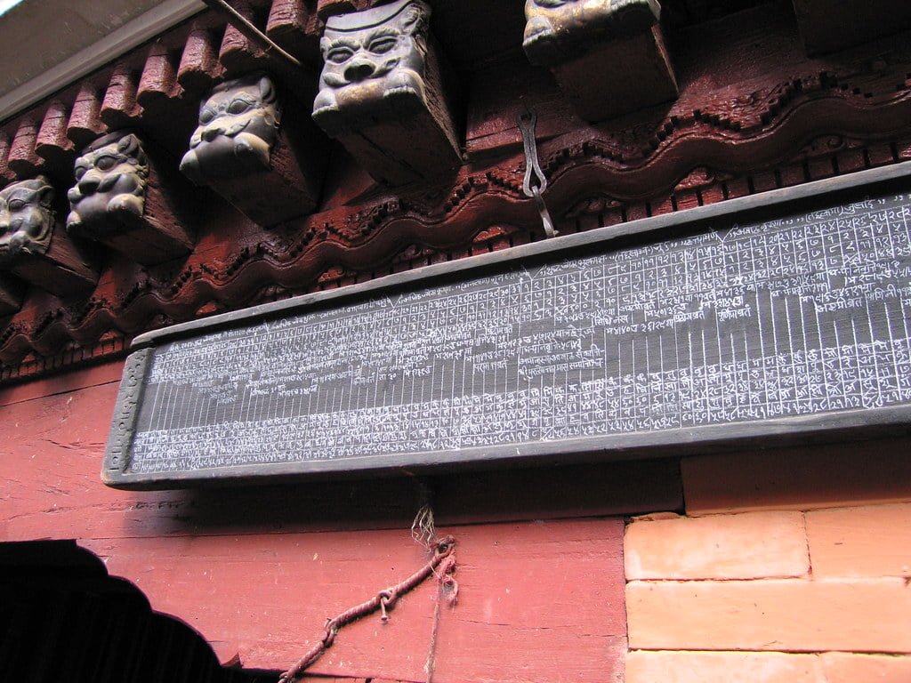A black stone tablet with intricate inscriptions hanging on a red wall, with traditional wooden carved faces above it.