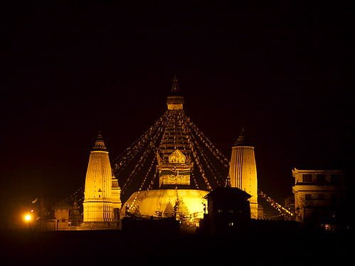 Illuminated temple at night with decorative lights outlining its structure and two domed buildings on either side.