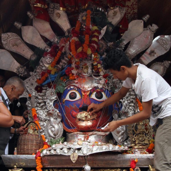 People engaging in a religious ceremony involving a large colorful deity mask decorated with flowers, fabrics, and metalwork.