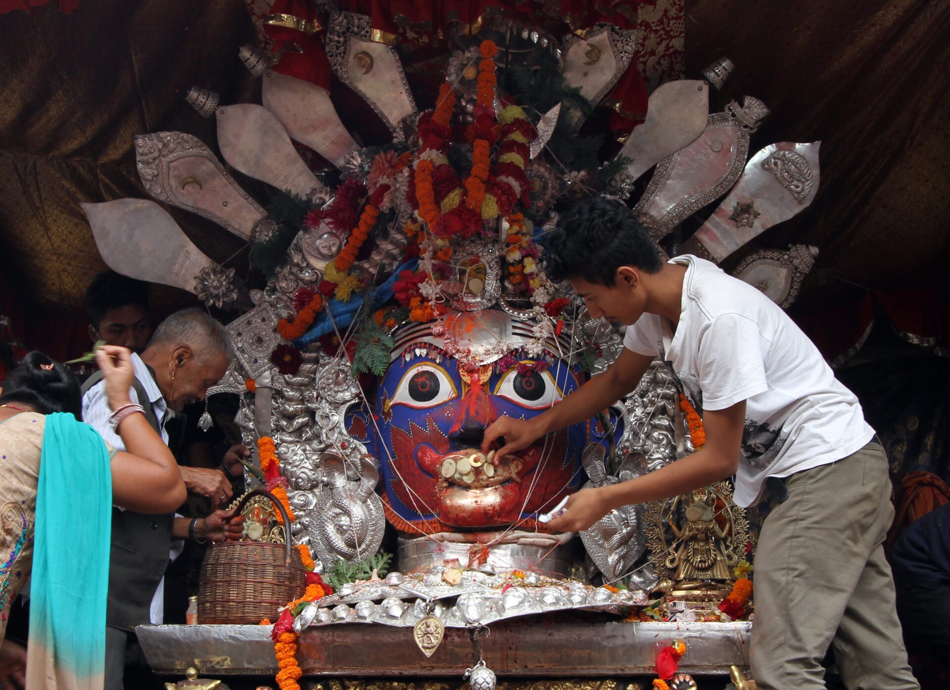 People engaging in a religious ceremony involving a large colorful deity mask decorated with flowers, fabrics, and metalwork.