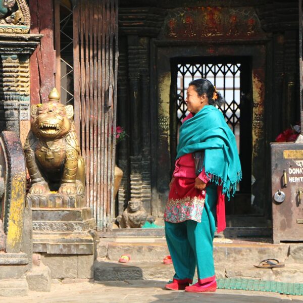 A woman in traditional attire stands in front of an ornate temple entrance, guarded by a gilded lion statue.