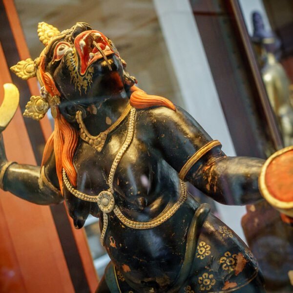 A detailed statue of a Hindu deity with dark blue skin, multiple arms, and ornate gold and red accents displayed behind a glass enclosure.