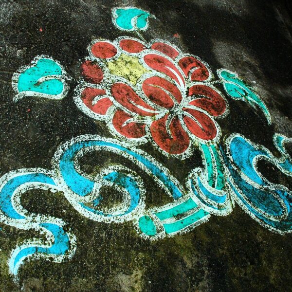 Colorful street art of a floral pattern with red, light blue, and white on a weathered concrete surface.