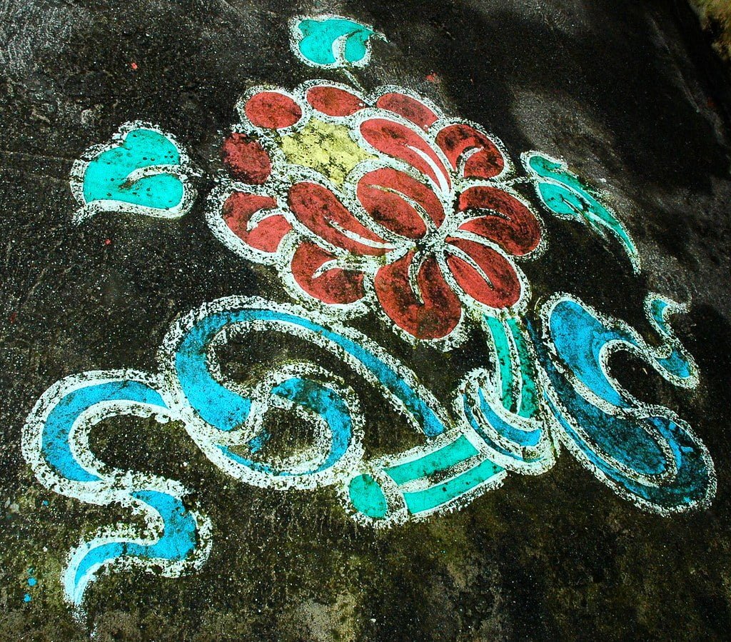 Colorful street art of a floral pattern with red, light blue, and white on a weathered concrete surface.