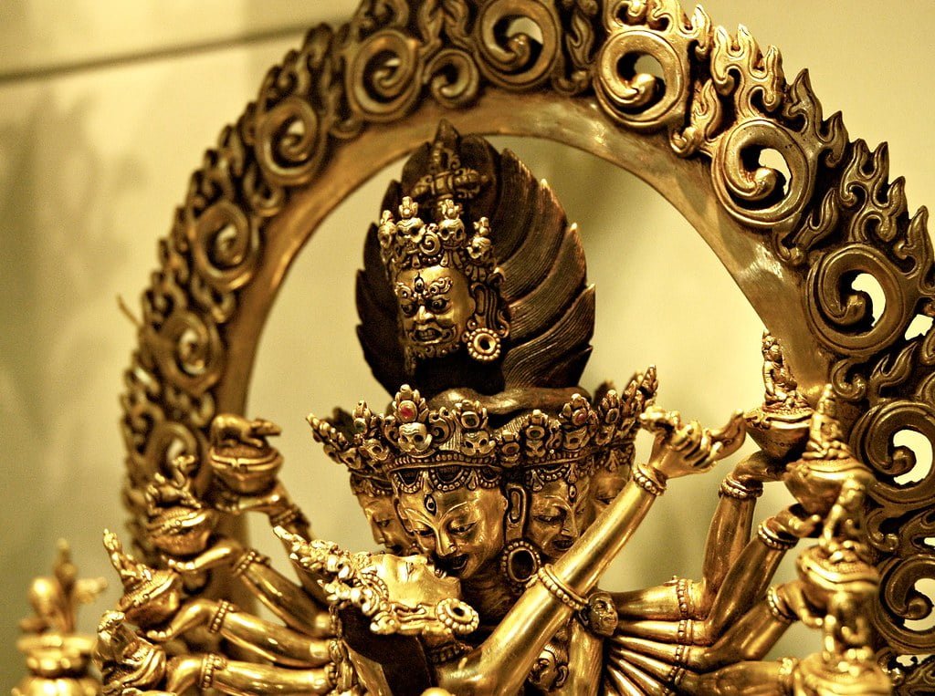 A detailed golden sculpture of a multi-faced and multi-armed deity set within an ornate circular aura.