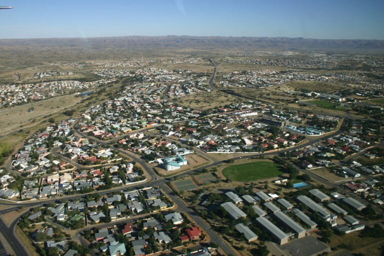 Aerial view of a sprawling suburban layout with curved roads, distinct residential and commercial areas, surrounded by arid landscape.
