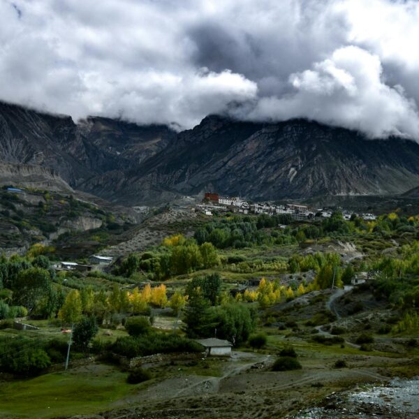 A small village nestled in a mountainous landscape with autumnal trees in the valley under a cloudy sky.
