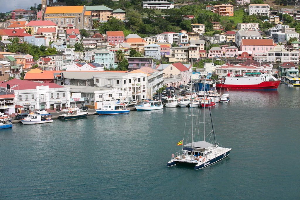 Aerial view of a coastal town with colorful buildings and a church, with various boats and a catamaran moored in the harbor.