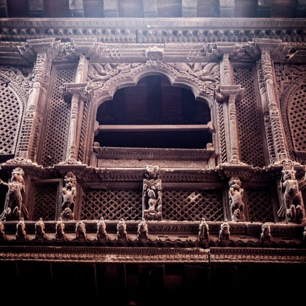 An intricately carved wooden facade featuring traditional motifs, patterns, and figures on a historical building, with dark tones and mood lighting highlighting the texture and craftsmanship.
