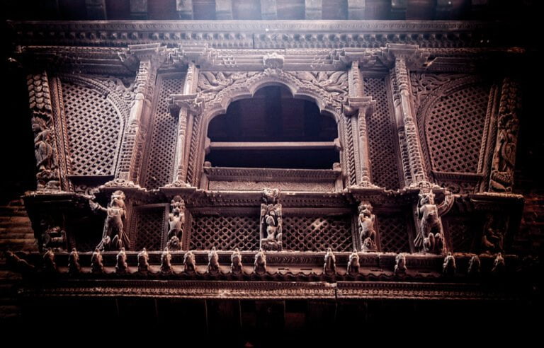 An intricately carved wooden facade featuring traditional motifs, patterns, and figures on a historical building, with dark tones and mood lighting highlighting the texture and craftsmanship.