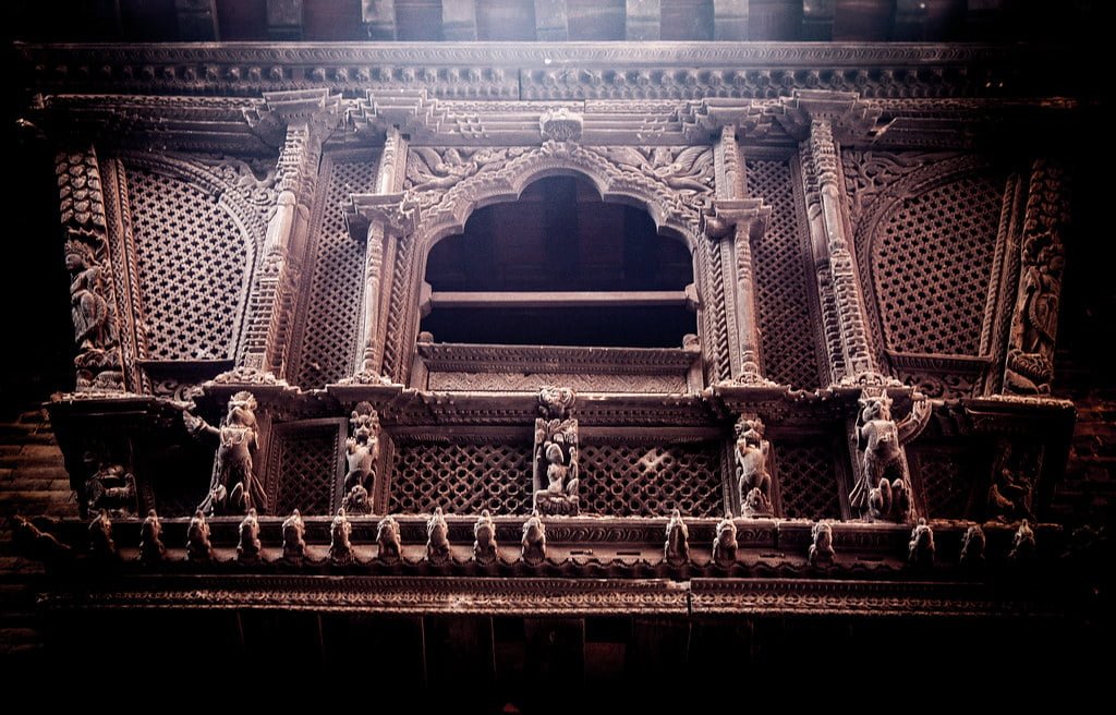 An intricately carved wooden facade featuring traditional motifs, patterns, and figures on a historical building, with dark tones and mood lighting highlighting the texture and craftsmanship.
