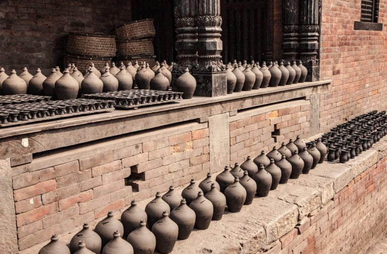 Rows of clay pots lined up on brick steps beside a traditional building with wooden carved details.