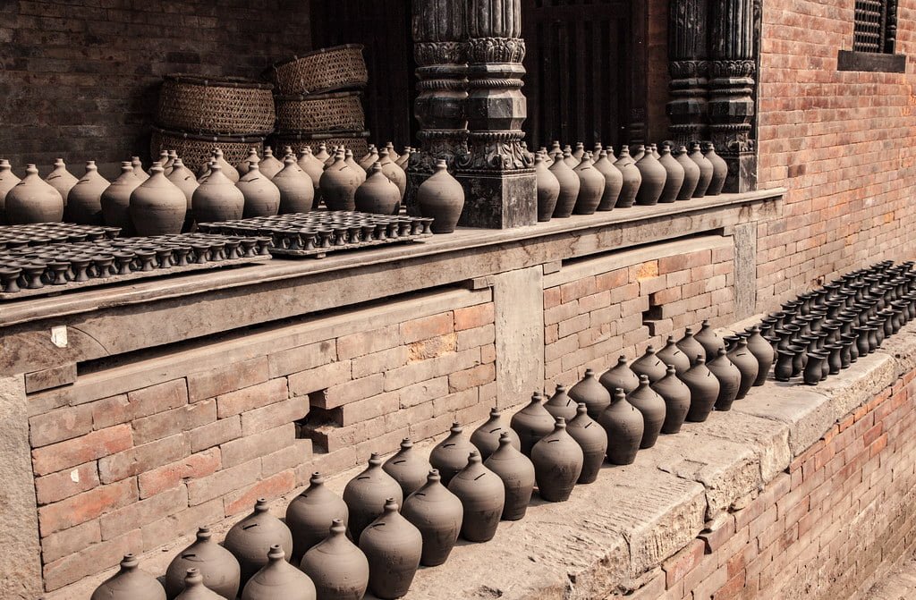Rows of clay pots lined up on brick steps beside a traditional building with wooden carved details.