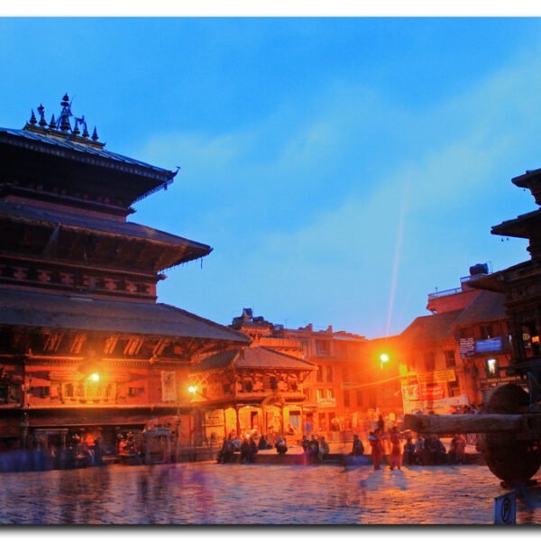 An evening view of two traditional multi-tiered temples at Durbar Square with people gathered and walking around in the blue hour light.