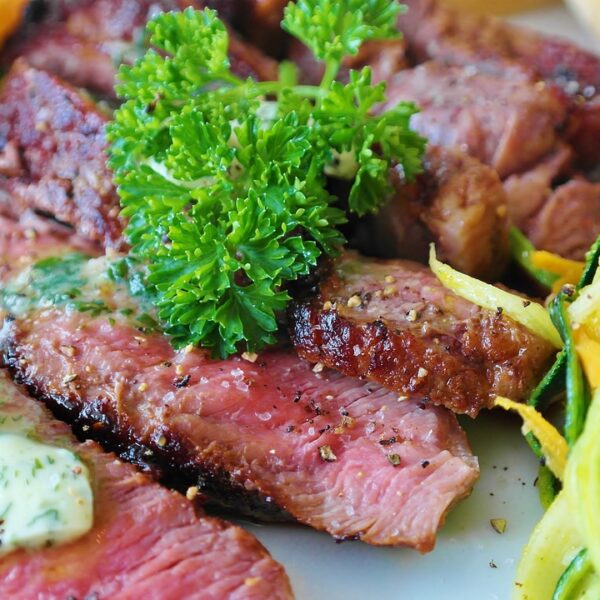 Sliced medium-rare steak topped with a dollop of herb butter and garnished with parsley, served with a side of spiralized vegetables.