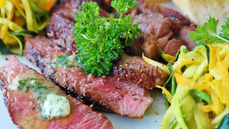 Sliced medium-rare steak topped with a dollop of herb butter and garnished with parsley, served with a side of spiralized vegetables.