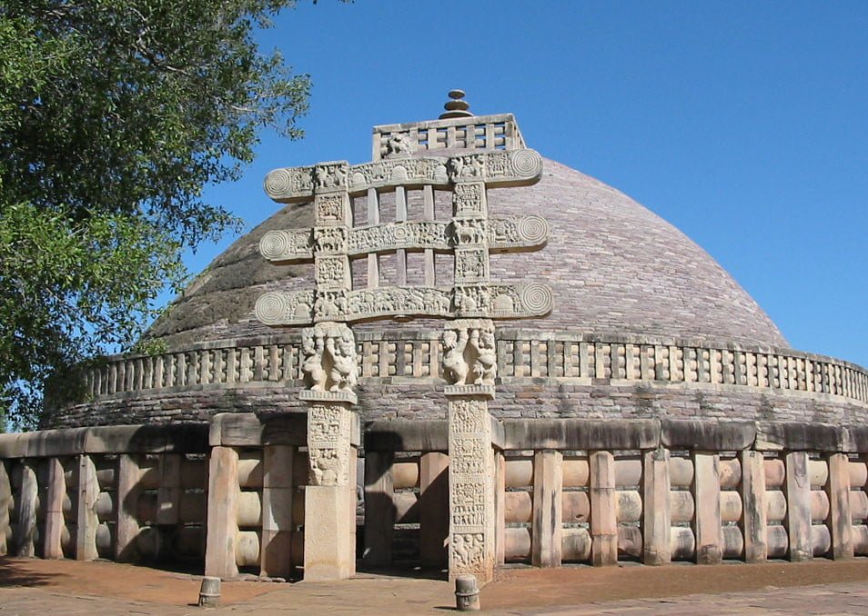 The Great Stupa at Sanchi, with its dome-shaped structure, ornate gateways, and intricate carvings against a clear blue sky.