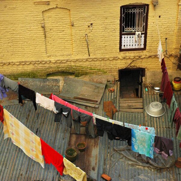 Aerial view of a rustic courtyard with clothes drying on lines between old buildings with weathered yellow walls and corrugated metal roofs.