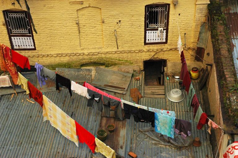 Aerial view of a rustic courtyard with clothes drying on lines between old buildings with weathered yellow walls and corrugated metal roofs.