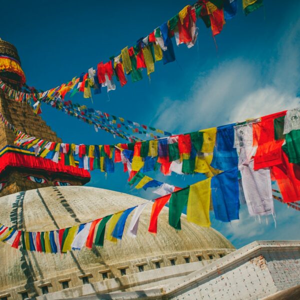 Colorful Tibetan prayer flags stretch across the sky above the Boudhanath Stupa, a UNESCO World Heritage Site, under a clear blue sky.