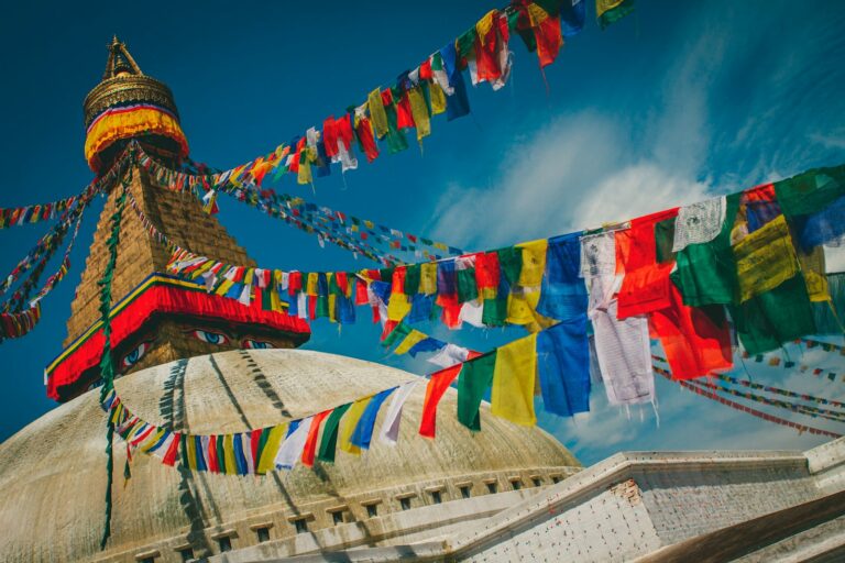 Colorful Tibetan prayer flags stretch across the sky above the Boudhanath Stupa, a UNESCO World Heritage Site, under a clear blue sky.