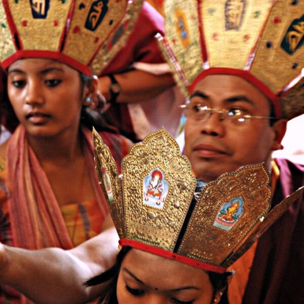 People wearing traditional Nepalese ceremonial hats with intricate designs participating in a cultural event.