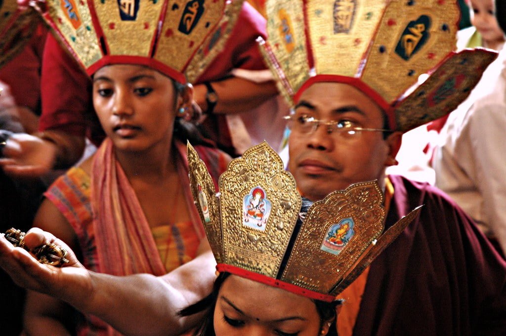 People wearing traditional Nepalese ceremonial hats with intricate designs participating in a cultural event.
