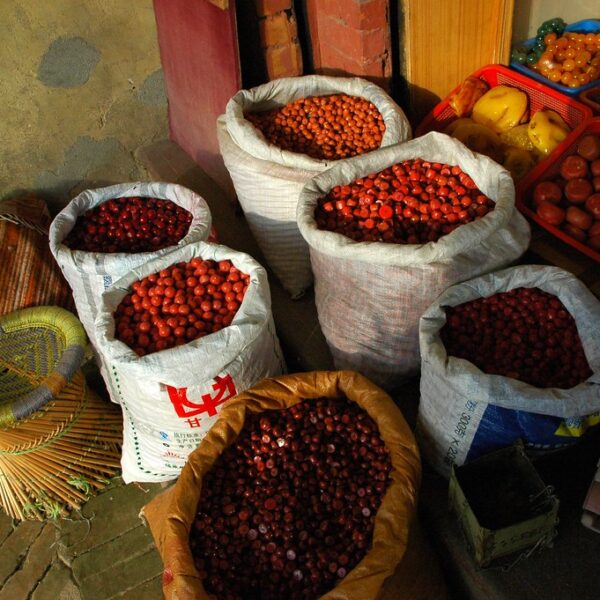 Sacks filled with chestnuts and plastic crates containing various fruits and vegetables displayed in front of a shop with a faded wall in the background.