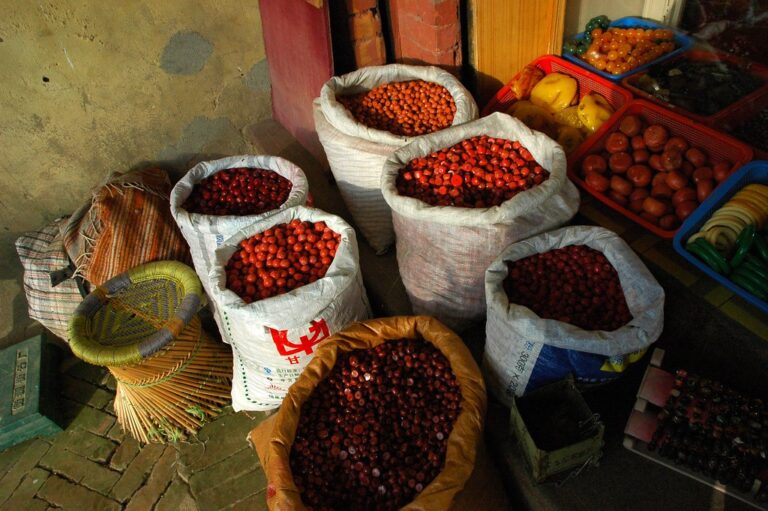 Sacks filled with chestnuts and plastic crates containing various fruits and vegetables displayed in front of a shop with a faded wall in the background.
