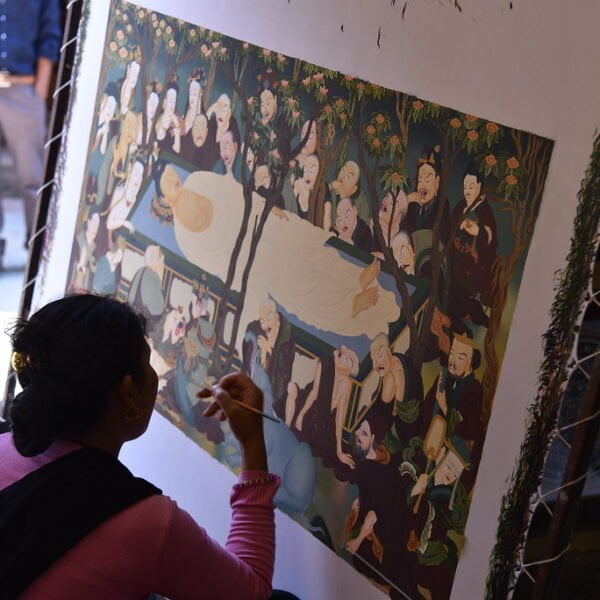 A person painting details on a large canvas with a traditional Asian-style artwork depicting multiple figures.
