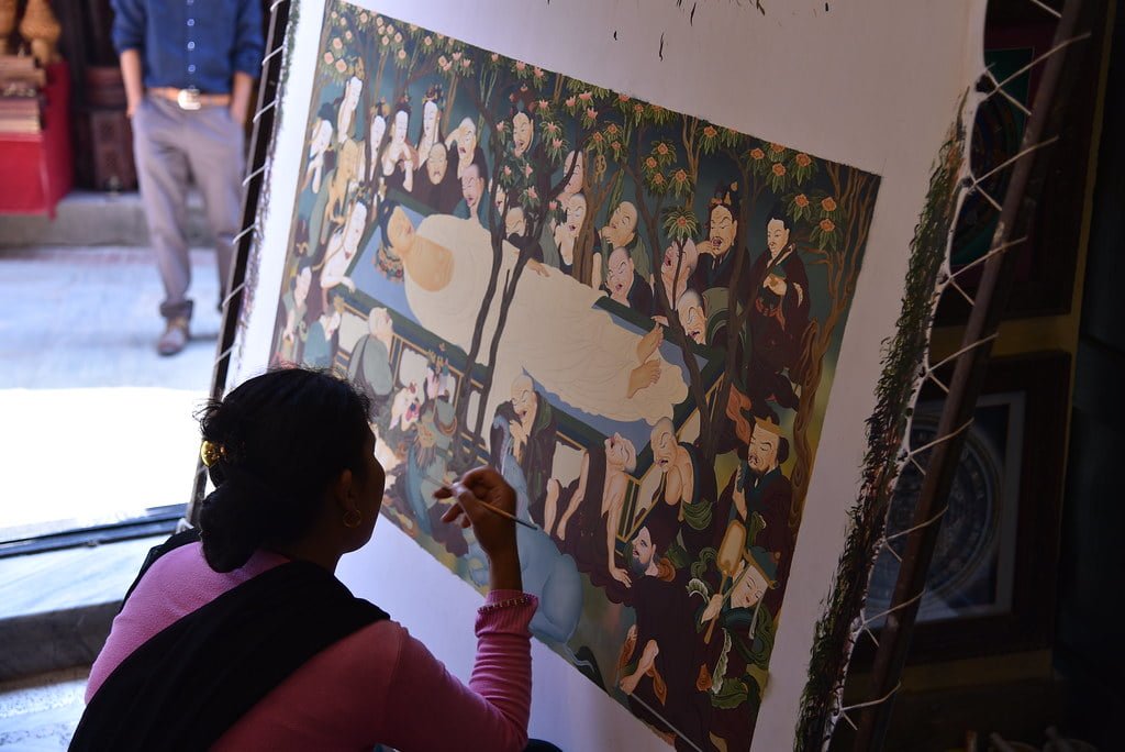 A person painting details on a large canvas with a traditional Asian-style artwork depicting multiple figures.