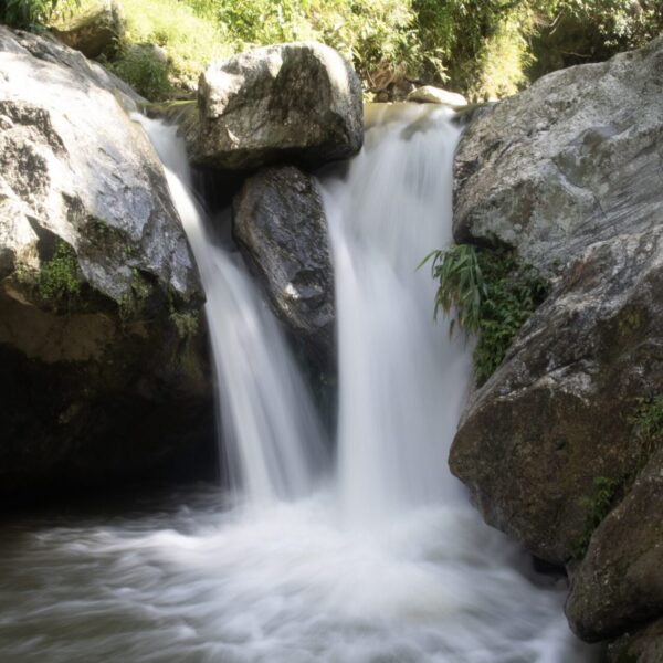 A small waterfall cascading between large rocks with a smooth, silky appearance of the water created by a long exposure photography technique, surrounded by green vegetation.
