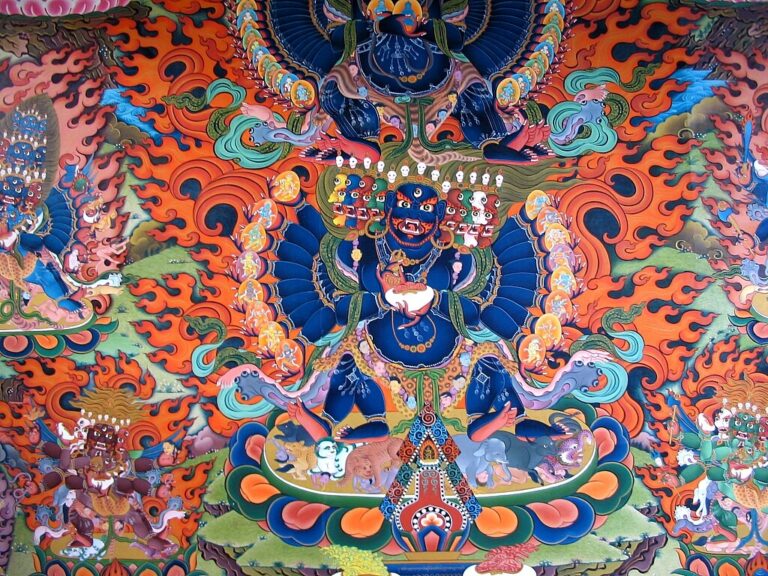A vibrant and detailed traditional Tibetan thangka painting featuring a blue deity surrounded by flames and smaller figures, with intricate patterns and a variety of colors.