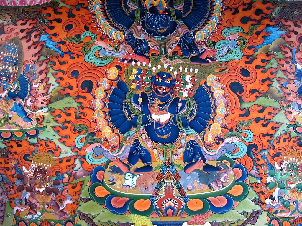 A vibrant and detailed traditional Tibetan thangka painting featuring a blue deity surrounded by flames and smaller figures, with intricate patterns and a variety of colors.