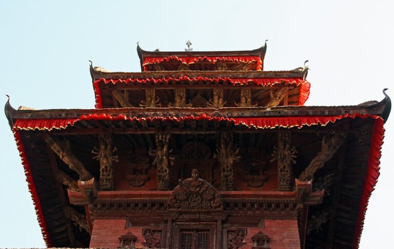 Alt text: A multi-tiered pagoda-style temple with intricate wood carvings and red fabric trimmings under a clear blue sky.