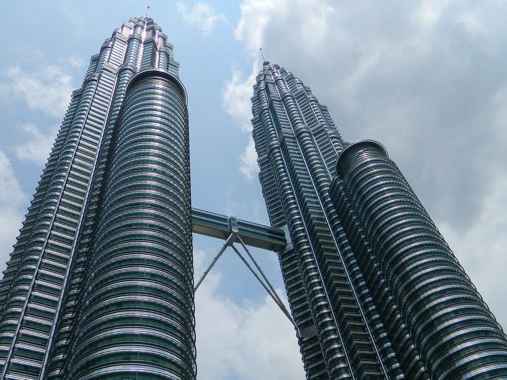 Two towering, curved skyscrapers connected by a skybridge against a cloudy sky.