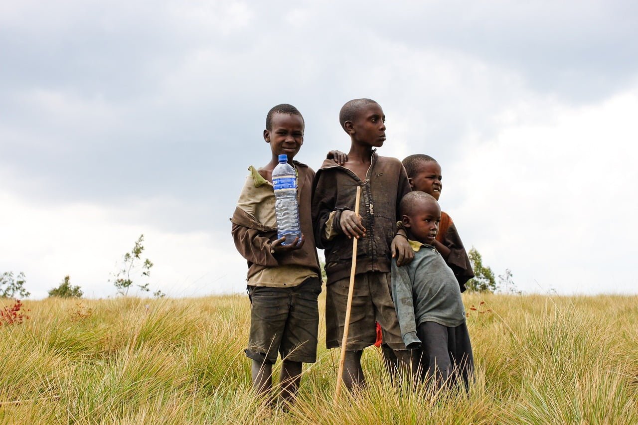 Four young boys standing in a grassy field with a cloudy sky in the background.